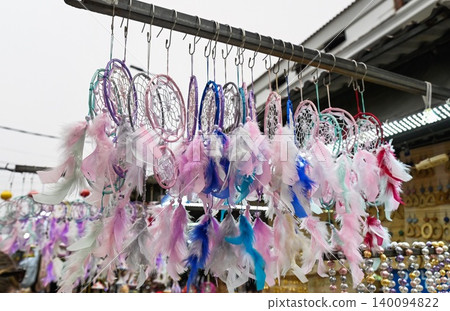 Row of handmade colorful dreamcatchers with pastel feathers hanging on metal bar at outdoor street souvenir market booth in Vietnam Row of handmade colorful dreamcatchers with pastel feathers hanging on metal bar at outdoor street souvenir market booth in Vietnam 140094822