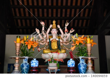 Beautiful multi armed Guanyin Bodhisattva statue sitting on lotus altar with orange lily flowers at a temple in Vietnam Beautiful multi armed Guanyin Bodhisattva statue sitting on lotus altar with orange lily flowers at a temple in Vietnam 140094859