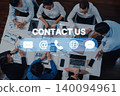 Diverse Business Team Collaborating Over Table with Digital Contact Us Icons and Communication Devices in Modern Office Setting Trope 140094961