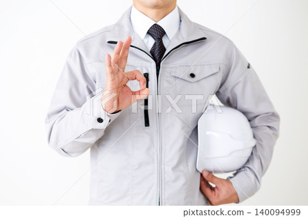 身穿灰色工作服的中年商人,手持頭盔,在白色背景前比劃著圓形手勢。 身穿灰色工作服的中年商人,手持頭盔,在白色背景前比劃著圓形手勢。 140094999