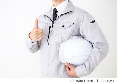 A middle-aged businessman in gray work clothes, holding a helmet and giving a thumbs-up, against a white background. A middle-aged businessman in gray work clothes, holding a helmet and giving a thumbs-up, against a white background. 140095065