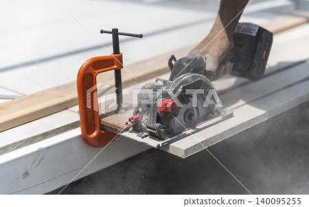Worker cutting smart board with a circular saw and orange C-clamp holding it in place. Worker cutting smart board with a circular saw and orange C-clamp holding it in place. 140095255