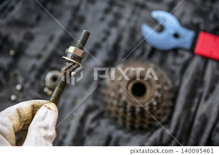 Bicycle repair process, focusing on a threaded axle with locknuts and blurred bike cassette background. Bicycle repair process, focusing on a threaded axle with locknuts and blurred bike cassette background. 140095461