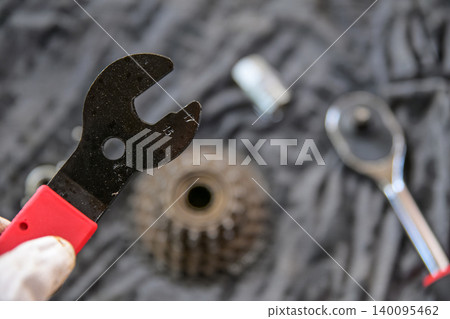 Specialty bike repair tool, cone spanner held by hand for bicycle wheel hub adjustment. a bicycle cone wrench with a blurred bike wheel hub background. Specialty bike repair tool, cone spanner held by hand for bicycle wheel hub adjustment. a bicycle cone wrench with a blurred bike wheel hub background. 140095462