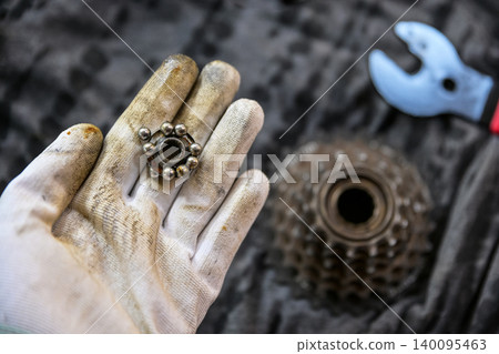 Technician wearing a stained white glove, showing broken or worn out bicycle hub bearings. Technician wearing a stained white glove, showing broken or worn out bicycle hub bearings. 140095463