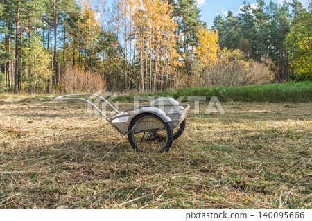 Garden cart in a field of dry grass with autumn trees in the background, outdoor scene Garden cart in a field of dry grass with autumn trees in the background, outdoor scene 140095666