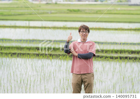 A farmer standing on the embankment of a rice paddy. A farmer standing on the embankment of a rice paddy. 140095731