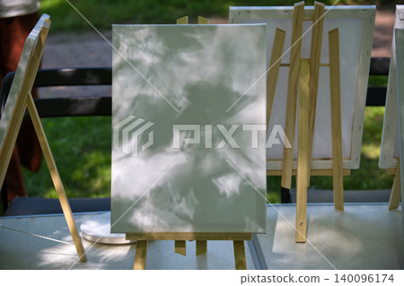 Blank canvases on wooden easels outdoors with dappled sunlight and shadows Blank canvases on wooden easels outdoors with dappled sunlight and shadows 140096174
