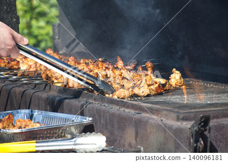 Hand using tongs to flip juicy meat skewers cooking on a hot outdoor barbecue grill Hand using tongs to flip juicy meat skewers cooking on a hot outdoor barbecue grill 140096181