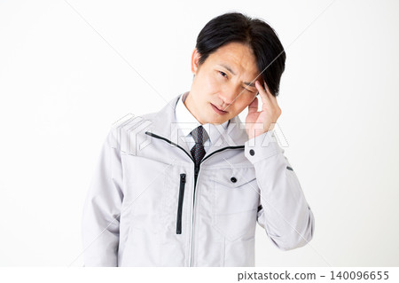 一位身穿灰色工作服的中年商人,在白色背景前,正忍受著頭痛的折磨。 一位身穿灰色工作服的中年商人,在白色背景前,正忍受著頭痛的折磨。 140096655