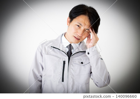 A middle-aged businessman in gray work clothes suffering from a headache, against a white background. A middle-aged businessman in gray work clothes suffering from a headache, against a white background. 140096660