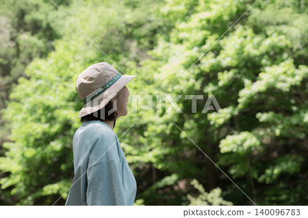 A woman enjoying the scenery while taking a walk in the forest; a faceless image showing her back as she enjoys the outdoors and summer camping. A woman enjoying the scenery while taking a walk in the forest; a faceless image showing her back as she enjoys the outdoors and summer camping. 140096783