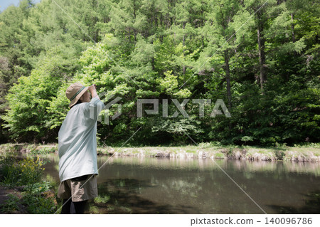 A woman enjoying the scenery while taking a walk in the forest; a faceless image showing her back as she enjoys the outdoors and summer camping. A woman enjoying the scenery while taking a walk in the forest; a faceless image showing her back as she enjoys the outdoors and summer camping. 140096786