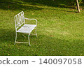 Vintage white metal garden chair on a lush green lawn in a peaceful backyard garden 140097058