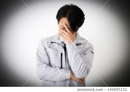 A middle-aged businessman in gray work clothes, holding his head in his hands in a daze, against a white background. A middle-aged businessman in gray work clothes, holding his head in his hands in a daze, against a white background. 140097232