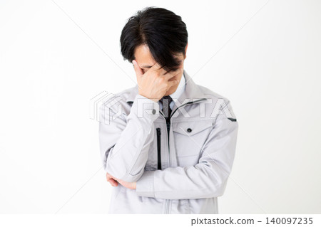 一位身穿灰色工作服的中年商人,雙手抱頭,神情恍惚,背景為白色。 一位身穿灰色工作服的中年商人,雙手抱頭,神情恍惚,背景為白色。 140097235