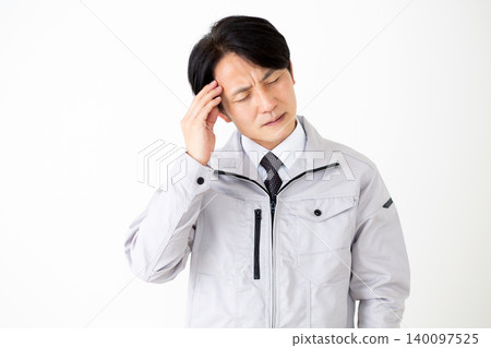一位身穿灰色工作服的中年商人,在白色背景前,正忍受著頭痛的折磨。 一位身穿灰色工作服的中年商人,在白色背景前,正忍受著頭痛的折磨。 140097525