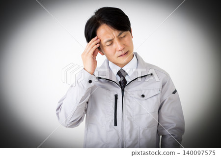 一位身穿灰色工作服的中年商人,在白色背景前,正忍受著頭痛的折磨。 一位身穿灰色工作服的中年商人,在白色背景前,正忍受著頭痛的折磨。 140097575