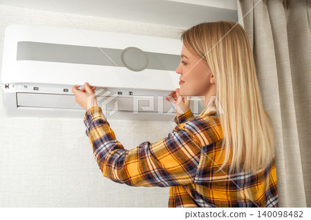 Woman inspects and maintains air conditioner in cozy indoor space Woman inspects and maintains air conditioner in cozy indoor space 140098482