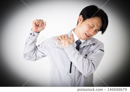 A middle-aged businessman in gray work clothes suffering from stiff shoulders, against a white background. A middle-aged businessman in gray work clothes suffering from stiff shoulders, against a white background. 140098679