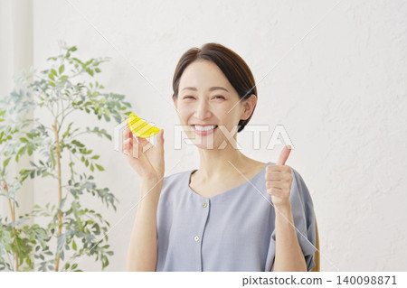 一位女士在客廳豎起大拇指，手裡拿著一個橘子。 140098871