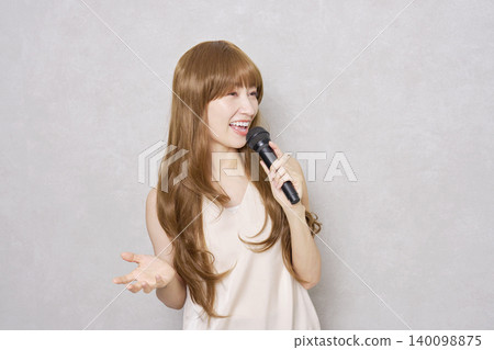 Middle-aged woman singing with a microphone, portrait, gray background Middle-aged woman singing with a microphone, portrait, gray background 140098875