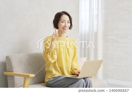 一位中年婦女豎起大拇指；一台筆記型電腦；客廳。 140098887