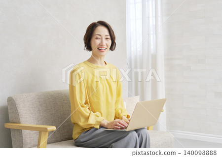 一位女士在客廳使用電腦，肖像照，她正看著鏡頭。 140098888