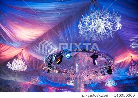 Luxurious wedding reception ceiling with crystal chandeliers and colorful lighting Luxurious wedding reception ceiling with crystal chandeliers and colorful lighting 140099069