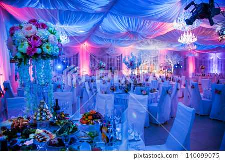 Luxurious wedding reception hall with elaborate floral decor and vibrant lighting Luxurious wedding reception hall with elaborate floral decor and vibrant lighting 140099075