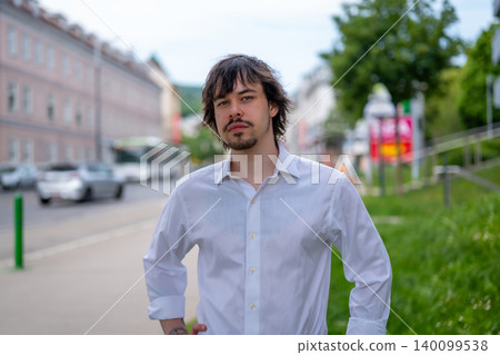 Portrait of young man with beard and long hair against city background. Portrait of young man with beard and long hair against city background. 140099538