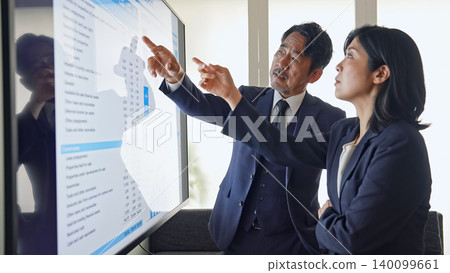 一群商務人士一邊看著螢幕一邊交談。 一群商務人士一邊看著螢幕一邊交談。 140099661