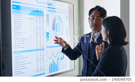A group of business people conversing while looking at a screen. A group of business people conversing while looking at a screen. 140099705
