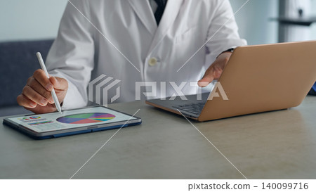 A man in a white coat working with a laptop and a tablet PC. A man in a white coat working with a laptop and a tablet PC. 140099716