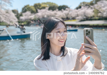 A young woman enjoys cherry blossom viewing from a boat at Chidorigafuchi, taking selfies with her smartphone. (Sightseeing/Date) A young woman enjoys cherry blossom viewing from a boat at Chidorigafuchi, taking selfies with her smartphone. (Sightseeing/Date) 140099762
