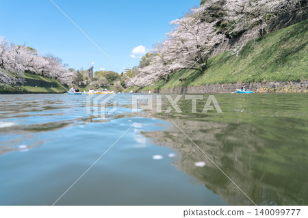 A clear blue sky and the cherry blossom trees lining Chidorigafuchi, with a lively scene of people enjoying cherry blossom viewing from boats on the water. A clear blue sky and the cherry blossom trees lining Chidorigafuchi, with a lively scene of people enjoying cherry blossom viewing from boats on the water. 140099777