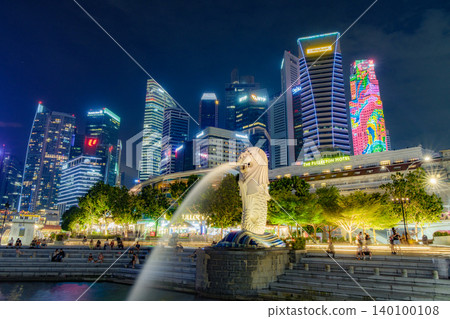 Tourist beside the Merlion statue fountain, iconic symbol of Singapore, overlooking the Marina Bay waterfront in the night Tourist beside the Merlion statue fountain, iconic symbol of Singapore, overlooking the Marina Bay waterfront in the night 140100108