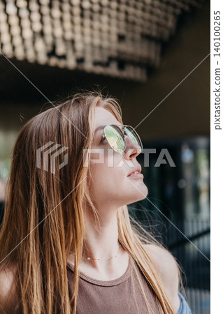 Woman wearing sunglasses looks upward in profile view against architectural background. Visionary mindset, urban perspective, future outlook. Woman wearing sunglasses looks upward in profile view against architectural background. Visionary mindset, urban perspective, future outlook. 140100265