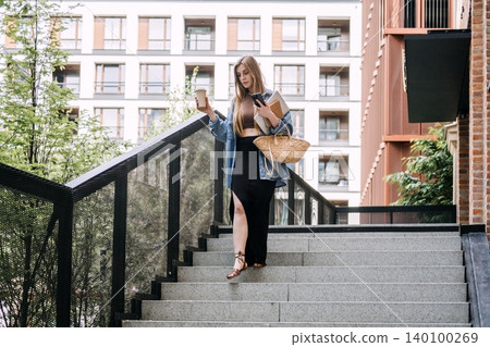 Woman walks down outdoor city staircase while holding coffee cup and smartphone. Freelancer on the move, digital nomad daily routine, remote work lifestyle. Woman walks down outdoor city staircase while holding coffee cup and smartphone. Freelancer on the move, digital nomad daily routine, remote work lifestyle. 140100269