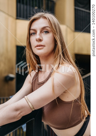 Woman leans on railing outside modern building looking directly at camera. Empowered women concept, self assured expression, authentic portraiture. Woman leans on railing outside modern building looking directly at camera. Empowered women concept, self assured expression, authentic portraiture. 140100270