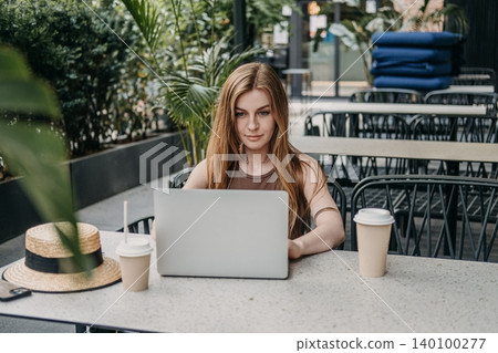 Woman types on laptop computer while sitting at outdoor cafe table. Freelance writer blogger, independent contractor job, working online terrace. Woman types on laptop computer while sitting at outdoor cafe table. Freelance writer blogger, independent contractor job, working online terrace. 140100277