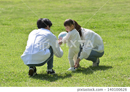 一對年輕夫婦和他們心愛的女兒在公園草坪上放鬆休息。 140100626