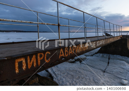 A rusty metal pier extends over a frozen lake at dusk, faded warning text A rusty metal pier extends over a frozen lake at dusk, faded warning text 140100698