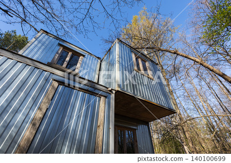 Stacked metal cabin modules rise among leafless trees beneath a clear blue sky Stacked metal cabin modules rise among leafless trees beneath a clear blue sky 140100699