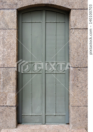 A muted green arched metal door set into a rough granite stone frame A muted green arched metal door set into a rough granite stone frame 140100703