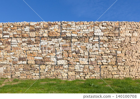 A rustic stone gabion retaining wall secured with wire mesh, background photo texture A rustic stone gabion retaining wall secured with wire mesh, background photo texture 140100708