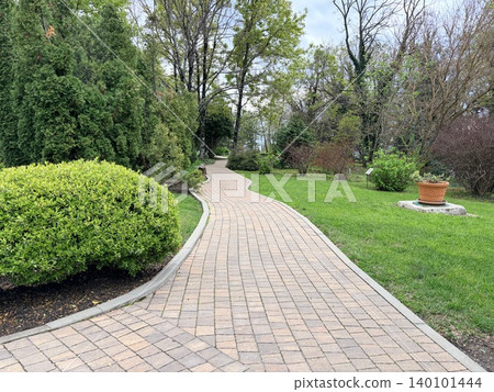 a winding paved walkway constructed from light tan rectangular pavers, bordered by a concrete curb. a winding paved walkway constructed from light tan rectangular pavers, bordered by a concrete curb. 140101444