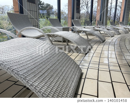 A row of white wicker sun loungers arranged along the curved edge of an indoor pool or spa area. A row of white wicker sun loungers arranged along the curved edge of an indoor pool or spa area. 140101458
