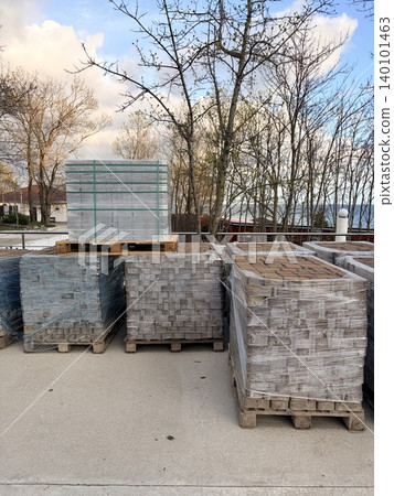 several stacks of construction materials, specifically paving stones or bricks, resting on wooden pallets on a concrete surface. several stacks of construction materials, specifically paving stones or bricks, resting on wooden pallets on a concrete surface. 140101463