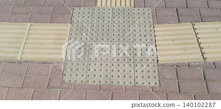 close up of tactile paving with raised dots bars on sidewalk for visually impaired pedestrians. textured surface ensures safety accessibility in urban environment close up of tactile paving with raised dots bars on sidewalk for visually impaired pedestrians. textured surface ensures safety accessibility in urban environment 140102287